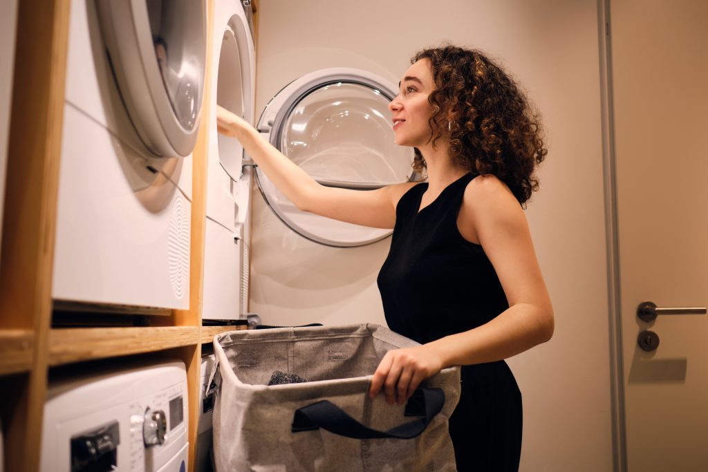 attractive-brunette-girl-dreamily-loading-clothes-into-washing-machine-modern-self-service-laundry
