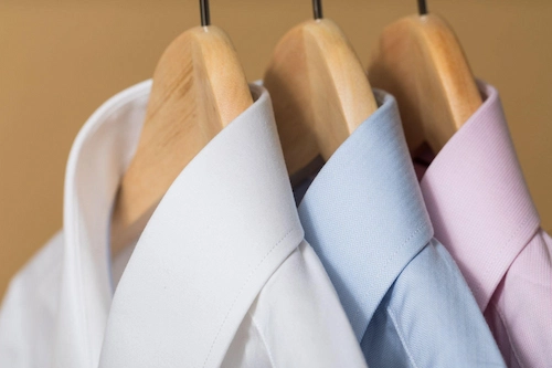 Closeup view of white, blue, and light pink shirts on hangers