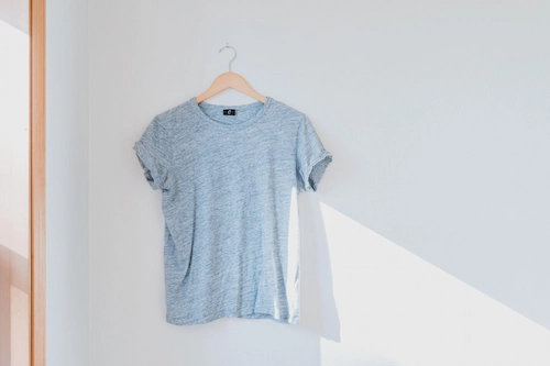Light blue lady’s t-shirt on a hanger hanging over a nail in the wall