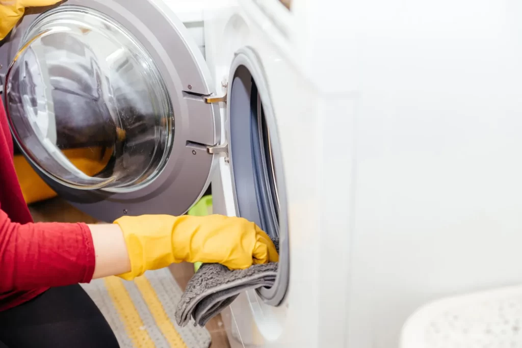Woman wearing protective yellow gloves and cleaning front load washing machine