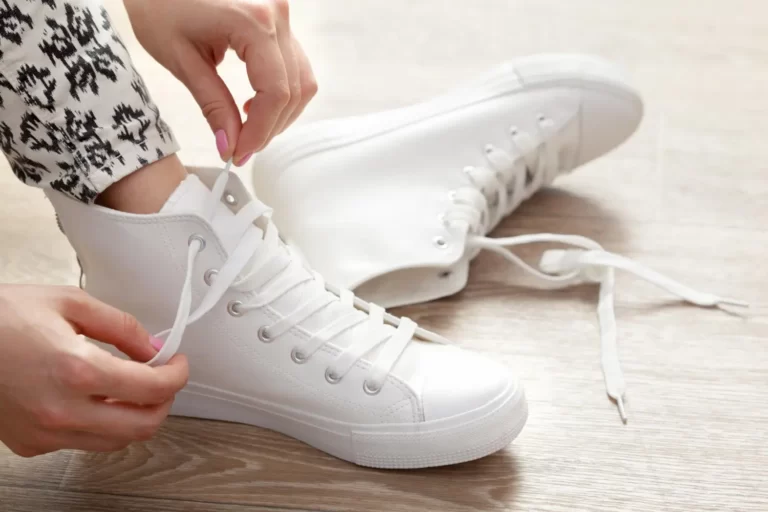A lady untying her white shoe laces.