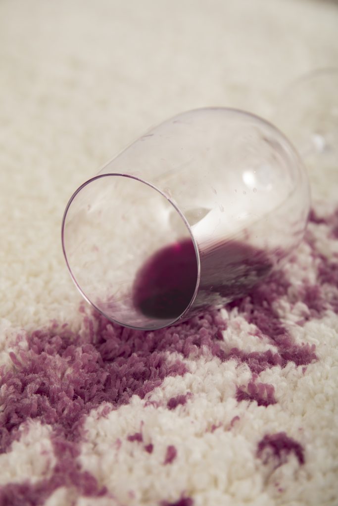 Red-wine-stain-on-a-pearl-white-rug-and-a-hand-with-soapy-sponge-cleaning-it